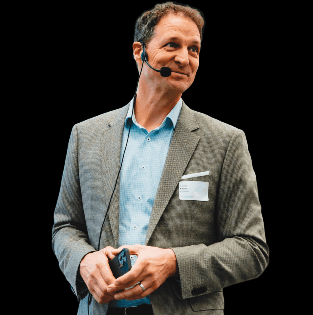 Carsten Kettler, Coach für Unternehmensnachfolge, im Gespräch bei einem Vortrag im Anzug, mit Mikrofon und Smartphone in der Hand.